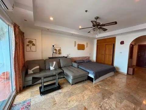Studio Condo for Sale at View Talay 5D living area with grey sectional sofa, bed, and wooden wardrobe
