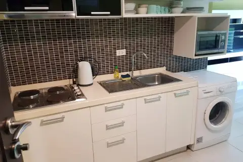 1 Bedroom Condo for Sale at Wongamat Privacy kitchen with electric hob, stainless steel sink, white cabinets, microwave, and washing machine