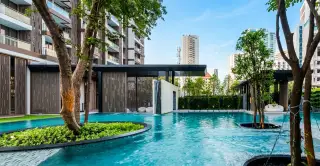 Baan Plai Haad large outdoor swimming pool with trees, modern building entrance, and city skyline.