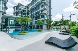 Sea Zen modern condo building with a large swimming pool, palm trees, sun loungers, and a poolside cabana.