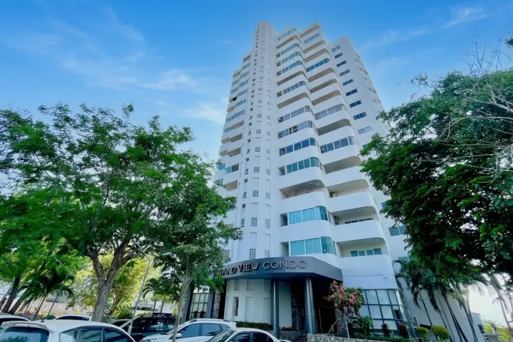 Grand View Condo exterior, a tall white building with curved balconies and blue windows, seen from a low angle surrounded by green trees.