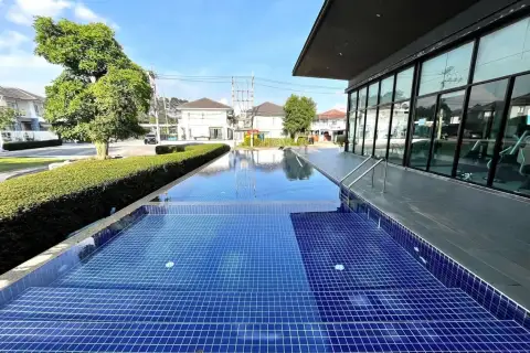 Baan Pruksa Nara Chaiyapruek modern fitness center with gym equipment and large windows overlooking a pool.