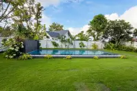 3 Bedroom House for Sale at Coco Ville 2 Pong - Bang Lamung large swimming pool surrounded by tropical trees and landscaped garden