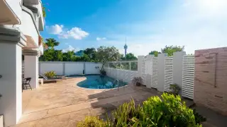 Little Norway Condominium outdoor swimming pool area with sun loungers, lush plants, and the building exterior.