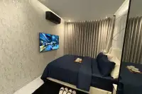 2 Bedroom Condo for Sale at Zenith Pattaya bedroom with wall-mounted TV, dark blue bed linen, and floor-to-ceiling curtains