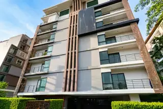 De Blue Condo exterior, a modern multi-story building with palm trees, hedges, and ground-level parking in Pattaya, Thailand.