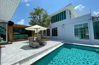 10 Bedroom House for Sale in Na Chom Thian: Exterior of light gray building with large windows, pool, and outdoor seating.