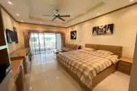 Studio Condo for Sale at Baan Suan Lalana spacious room with king bed, ceiling fan, sofa, and sliding doors to balcony