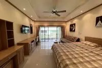 Studio Condo for Sale at Baan Suan Lalana bright studio room with king bed, wooden desk, wall-mounted TV, and balcony access