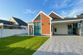 Pansuk Lakeside: Modern house exterior with brick and white facade, large windows, green lawn, and patterned driveway under cloudy sky.