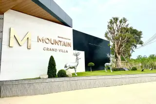 M Mountain Grand Villa entrance sign on a modern white and black building facade, with two silver deer statues on a green lawn.