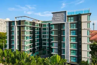 Siam Oriental Plaza exterior of modern condo building with lush tropical landscaping and palm trees under a clear sky.