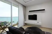 1 Bedroom Condo for Sale at Cetus Beachfront bright living room with leather sofa, wall-mounted TV, and floor-to-ceiling sea view window