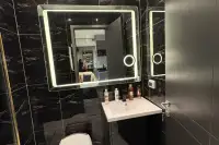 1 Bedroom Condo for Sale at Zenith Pattaya bathroom with large LED mirror, black marble wall tiles, and white sink vanity