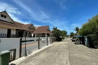 Dhewee Resort entrance gate with a small guardhouse, lush green trees, and a resort sign in Thai script.