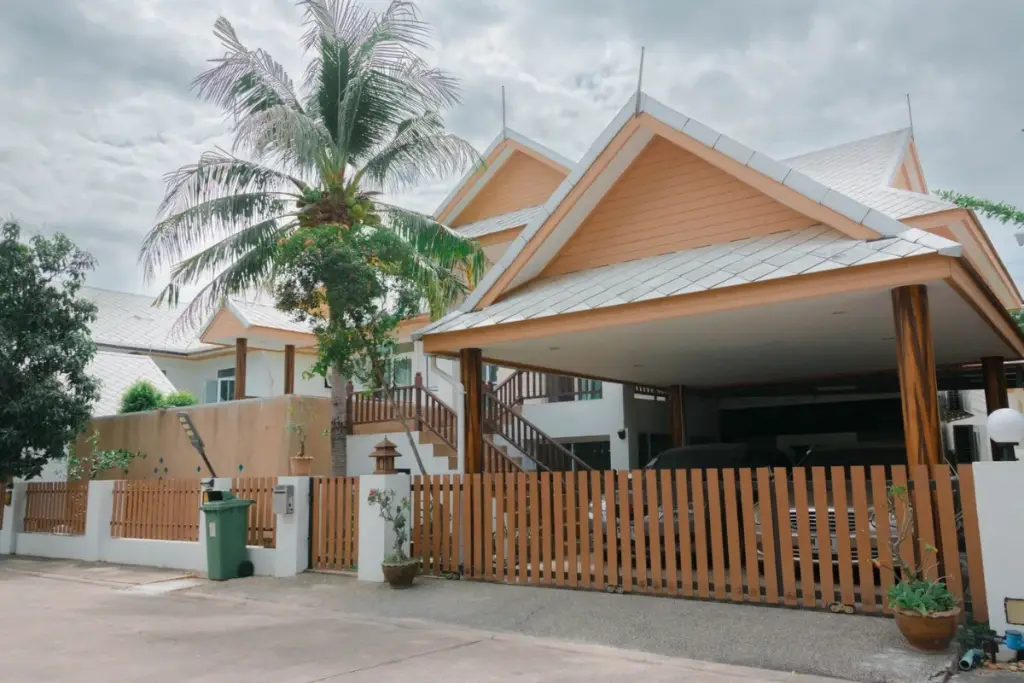 6 Bedroom House for Sale & Rent at Amorn Village, exterior view with carport, wooden fence, and palm tree.