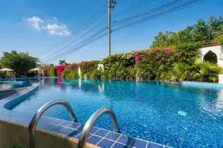 Sunrise Beach Residence large outdoor swimming pool with blue mosaic tiles, surrounded by lush greenery and flowering bushes.