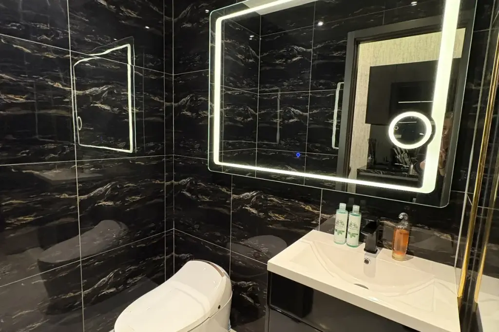 Studio Condo for Sale at Grand Solaire Noble luxury bathroom with black marble tiles, LED-lit mirror, and white basin vanity