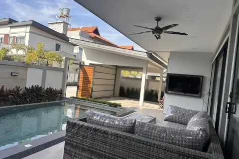 Zensiri Midtown Villas covered outdoor terrace with rattan sofa, poolside ceiling fan, wall-mounted TV and wooden entry gate