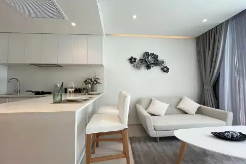1 Bedroom Condo for Sale at Celine Wongamat open-plan kitchen and living area with white bar counter, sofa, and floral wall art