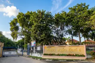 Pattaya Park Hill 4 entrance sign in Thai script, with green letters on a beige wall and trees in the background.