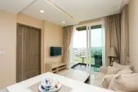 1 Bedroom Condo for Sale at Del Mare bright living room with beige sofa, wall-mounted TV, and floor-to-ceiling balcony doors with sea view
