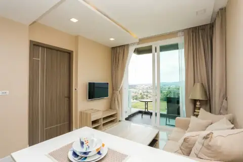 1 Bedroom Condo for Sale at Del Mare bright living room with beige sofa, wall-mounted TV, and floor-to-ceiling balcony doors with sea view
