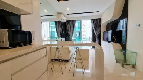 1 Bedroom Condo for Sale at City Center Residence living room with wall-mounted TV, breakfast bar, and city balcony view