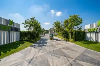 Cozy Ville entrance with security gate, modern signage, patterned driveway, and lush green landscaping.