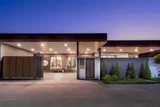 M Mountain Lake modern house exterior entrance with a large gate, covered carport, and landscaped front yard at dusk.