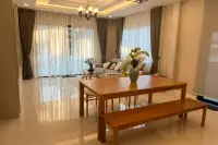 3 Bedroom House for Sale at SP Village 1 open-plan dining and living area with wooden table, bench seating and sheer curtains