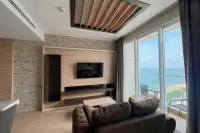1 Bedroom Condo for Sale at Cetus Beachfront living room with wooden TV wall, brown sofa and floor-to-ceiling sea view windows