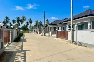 Lee Garden row of modern grey houses with dark roofs, red gates, and palm trees under a clear blue sky.