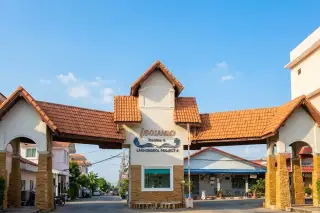 Eakmongkol 4 two-story yellow house with red tiled roof, ornate black and gold fence, and lush green landscaping.
