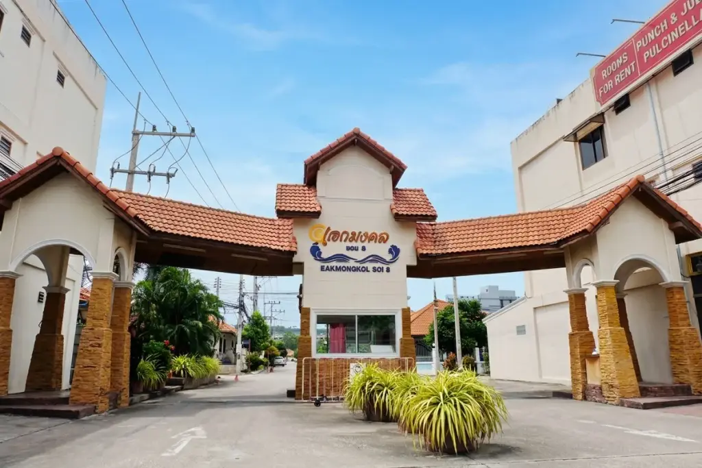 Eakmongkol 8 concrete residential street lined with trees in planters and green hedges, utility poles overhead.
