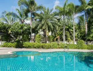 The Meadows large swimming pool with reflections of the clubhouse and tropical trees under a sunny sky.
