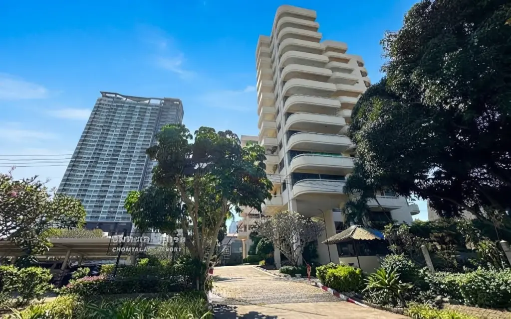 Chom Talay Resort exterior, showing the main building with curved balconies, lush trees, and a modern high-rise in the background.