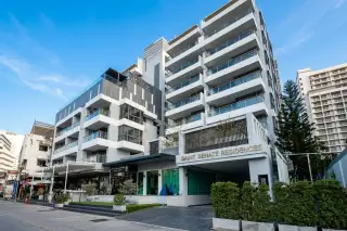The Senate Residences, a modern white and grey building exterior with glass balconies and ground-floor shops.