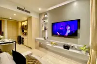 1 Bedroom Condo for Sale & Rent at Arom Wongamat: Living area with TV, sofa, and view towards modern kitchen and dining table.
