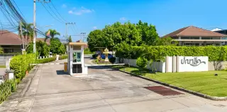 Baan Panalee entrance sign in Thai and English on a white wall with green grass and foliage.