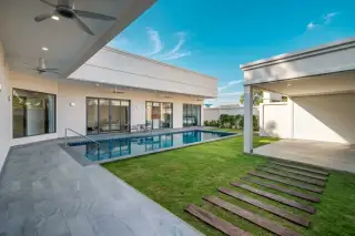 The Hacienda Villas modern exterior at dusk, featuring two illuminated garage doors, a wooden front door, concrete driveway, and green lawn.