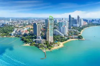 The Riviera Palm Beach: Aerial view of the tall, modern condo building on a sandy beach next to turquoise ocean, surrounded by city skyline.