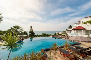Baan Rimpha infinity pool with ocean view, sun loungers, and a striped umbrella under a bright sky.