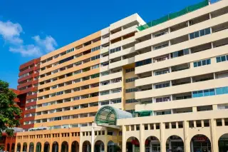Keha Thepprasit multi-story condo building with cream, orange, and red sections, arched ground floor shops, and a green covered walkway.