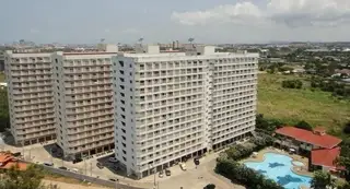 Jomtien Beach Condominium aerial view of multiple white buildings, a large swimming pool, and surrounding landscape.