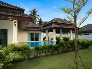Unique Paradise Resort backyard with a rectangular swimming pool, outdoor shower, covered patio, and green lawn.