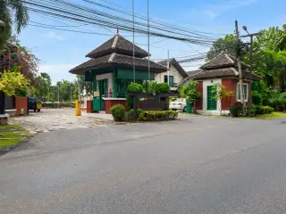 Mantara Village wide, paved street lined with tropical trees, houses, and power lines under a clear sky.