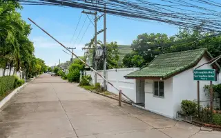 Baan Suan Suwattana Phase 2 entrance gate with security booth and barrier, leading to a residential street.