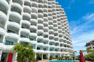 Star Beach Condotel white building with many curved balconies, a swimming pool, and palm trees under a blue sky.
