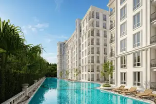 Harmonia City Garden long outdoor swimming pool with decorative paving, palm trees, and illuminated white condo buildings at dusk.
